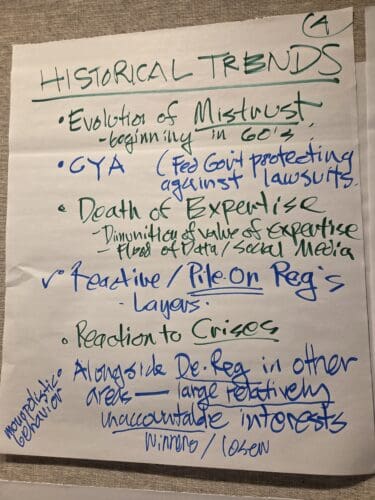 Handwritten poster titled 'Historical Trends' with green and blue bullet points about distrust and 'Death of Expertise'.